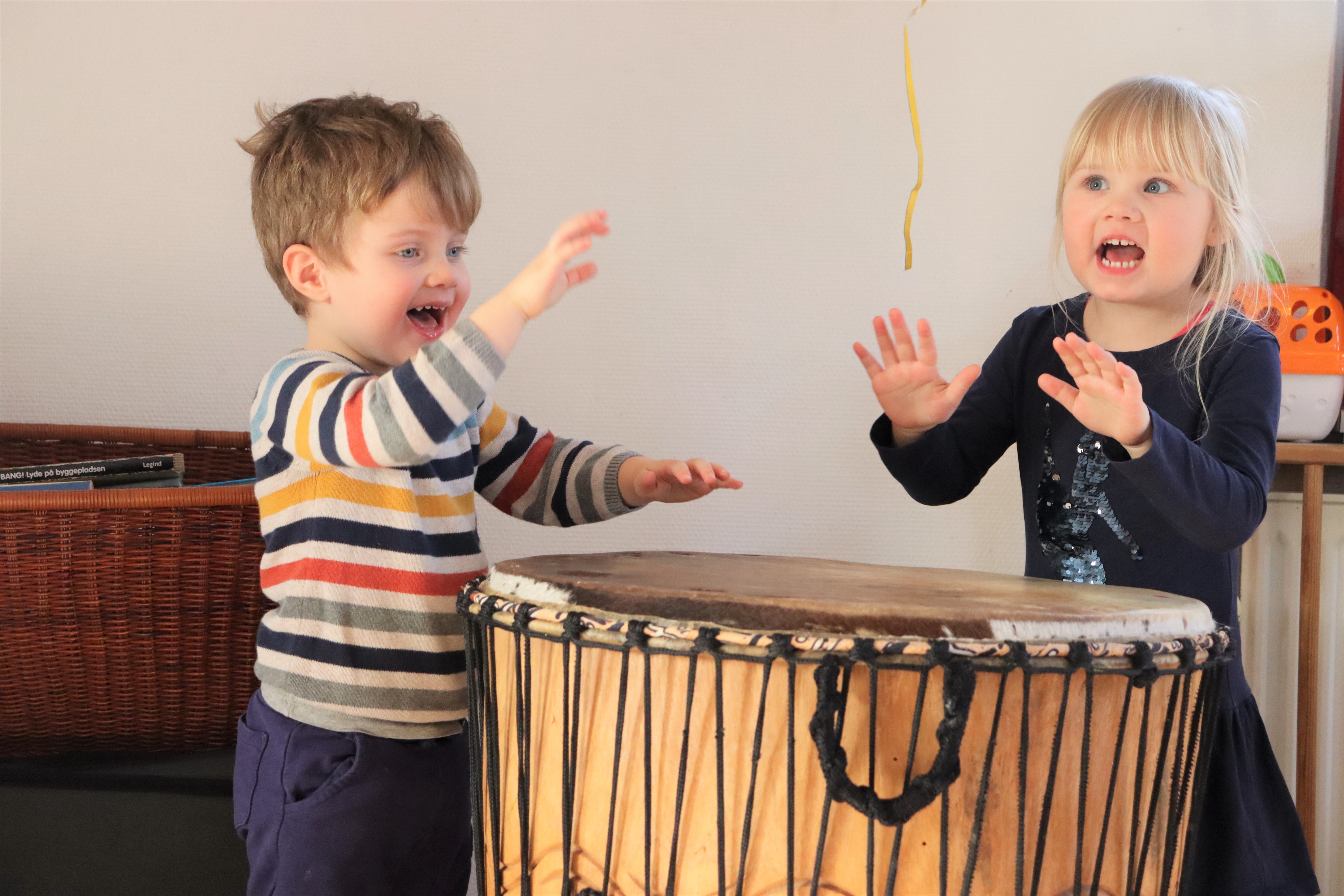 To børn står ved stor tromme, og trommer på den med deres hænder