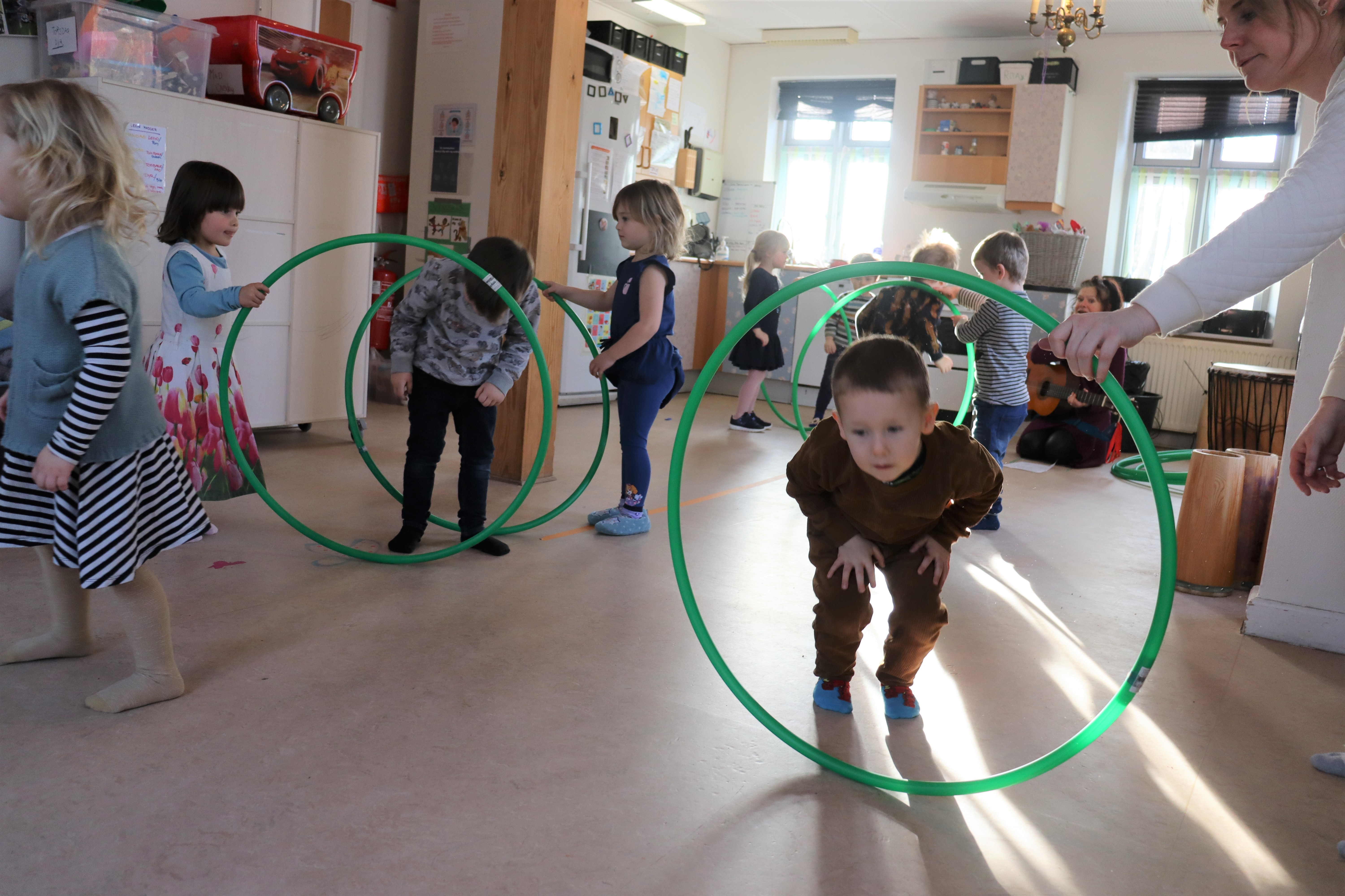 Børn kravler igennem hulahop ringe, som andre børn holder til musik
